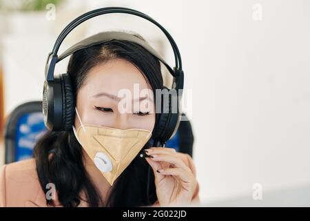 Young female call center manager in protective mask and headphones answering phone call of customer Stock Photo