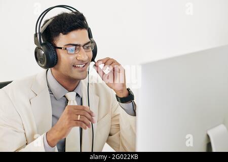 Positive excited young businessman wearing headset wheb having online meeting with colleagues Stock Photo