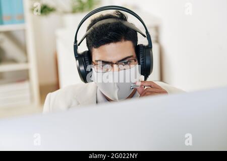 Serious technical support operator in medical mask and headphones answering phone call of customer Stock Photo