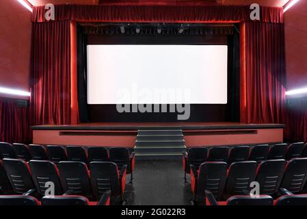 White blank screen in empty movie theater with rows of seats and red interior Stock Photo