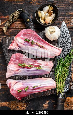 Raw lamb shanks meat on a cutting board with herbs. Dark wooden background. Top view Stock Photo