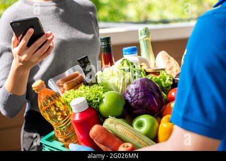Delivery man delivering groceries that ordered online to a woman customer at home, food delivery service in the time of pandemic concept Stock Photo