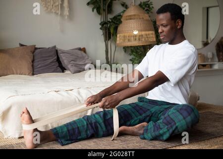 young african man sitting in janushirshasana seated forward bend posture at home Stock Photo