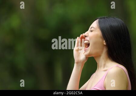 Profile of an asian woman shouting with hand on mouth in a park Stock Photo