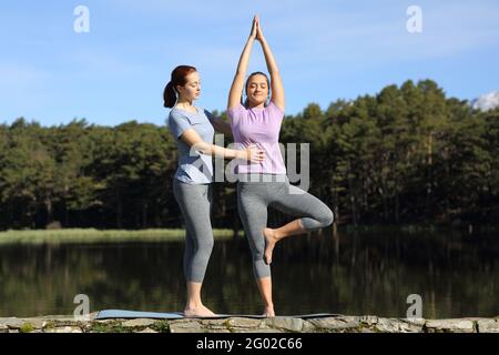 Front view portrait of a yogi teaching yoga to a woman in a lake Stock Photo