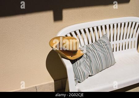 A cowboy wicker hat on a white bench with a striped vintage cushion in the garden (Marche, Italy, Europe) Stock Photo