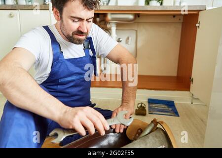 Do-it-yourselfer looks uncertainly at his tools to repair the defective kitchen sink Stock Photo