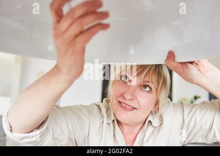 Handyman woman changes LED lightbulb on energy-saving lamp at home Stock Photo