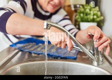 Handyman woman repairs kitchen sink faucet and checks water flow Stock Photo