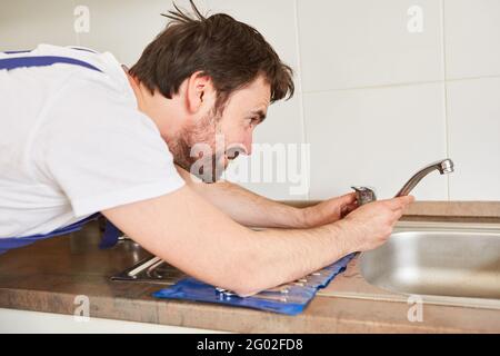 Plumber or handyman plumber repairs faucet on the sink in the kitchen Stock Photo