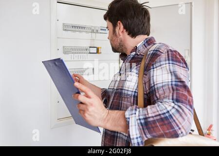 An electrician with a checklist checks the safety of the distribution box in an apartment Stock Photo