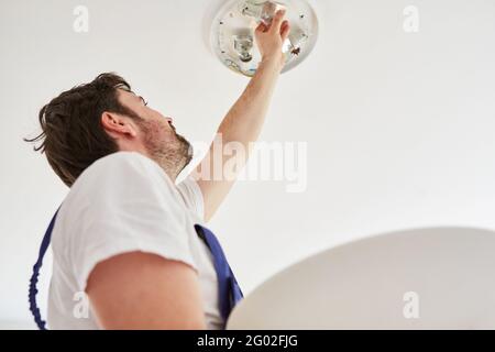 Electrician tradesman connects a ceiling lamp with several LED light bulbs Stock Photo