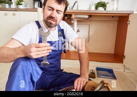Handyman unsafe holds a wrench while repairing the broken sink Stock Photo