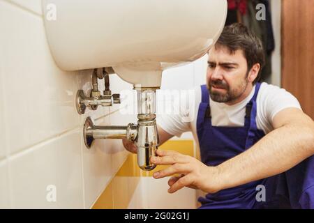 Plumber or handyman repairs siphon pipe on bathroom sink Stock Photo