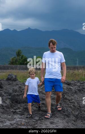 VERTICAL Serious Father son or adult younger brother walk together look for adventure. Cloudy sky before rain, mountain background. Man talk, hold boy Stock Photo