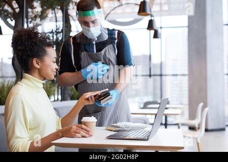 Portrait of waiter wearing face shield and gloves while serving customer in cafe with covid safety measures, copy space Stock Photo