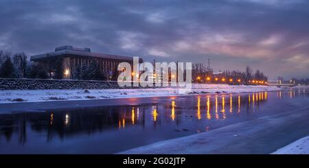 uzhhorod, ukraine - 26 DEC 2016: winter cityscape at dawn. beautiful scenery on the river uzh. city lights reflecting in the water. snow on the embank Stock Photo