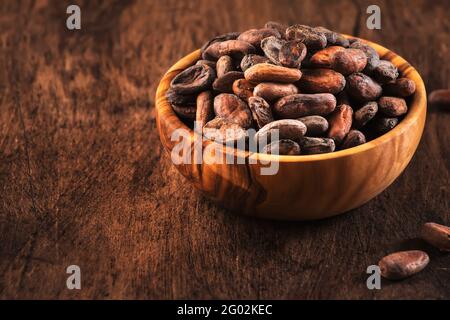 Unpeeled organic cocoa bean in bowl on wooden rustic table background. Copy space Stock Photo