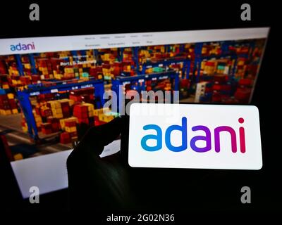 Person holding smartphone with logo of Indian conglomerate Adani Group on screen in front of website. Focus on phone display. Stock Photo