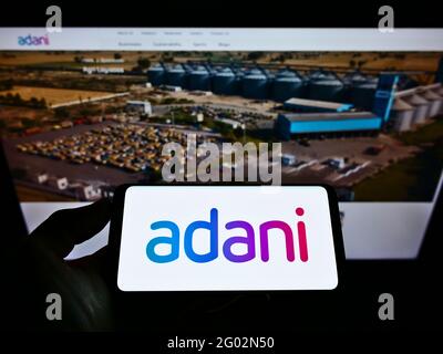 Person holding cellphone with company logo of Indian conglomerate Adani Group on screen in front of business website. Focus on phone display. Stock Photo