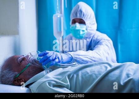 Doctor hazmat or protective suit helping to wear ventilation oxygen mask to covid infected difficulty in breathing to patient at hospital - Concept of Stock Photo