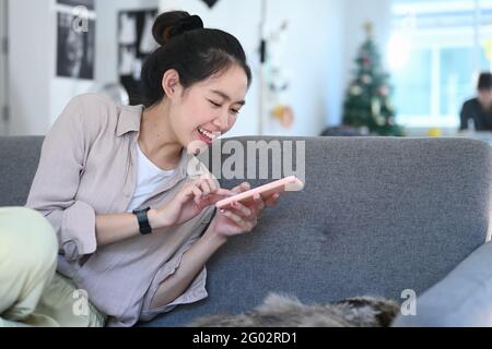 Happy young woman using smartphone taking a photo of cat on sofa. Stock Photo