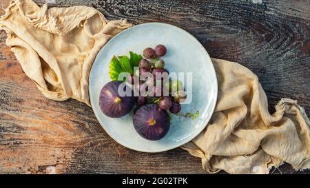 Figs and grapes in a plate on a wooden table Stock Photo