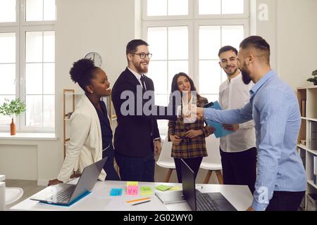 Male leader of a multiracial business team greets a new team member shaking his hand. Stock Photo