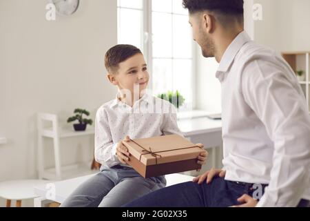 Smiling preteen son congratulating giving to loving father wrapped gift box Stock Photo