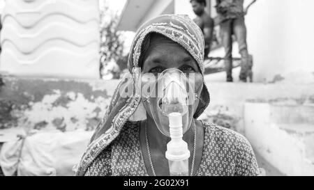 20 May 2021- Reengus, Sikar, India. Old Indian woman infected with Covid 19 disease. Patient inhaling oxygen wearing mask with liquid Oxygen flow. Stock Photo