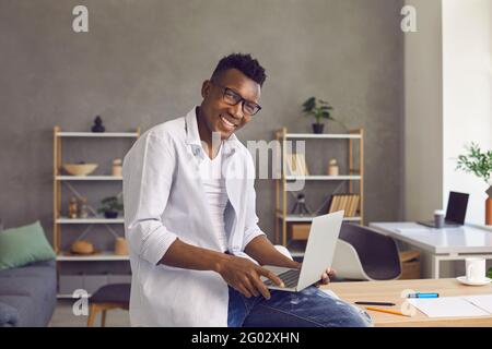 Happy smart african american man with laptop sitting on desk looking at camera Stock Photo