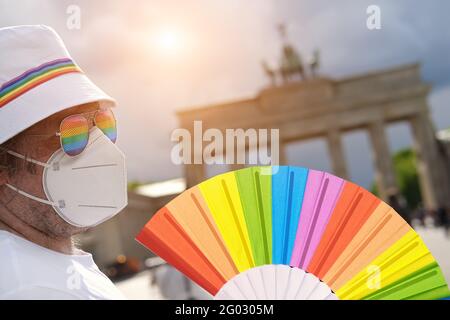 Mature Caucasian LGBT man in Berlin with rainbow fan and ribbon on white summer hat. Rainbow, symbol of LGBTQIA gay pride, diversity. Male activist is Stock Photo