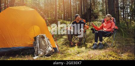 forest camping - young hiker couple enjoying cup of tee at campsite Stock Photo