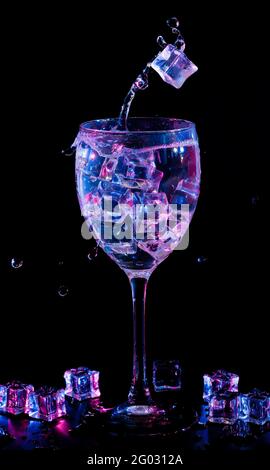Ice cubes falling into a wineglass with liquid. Two-color backlight. Stock Photo