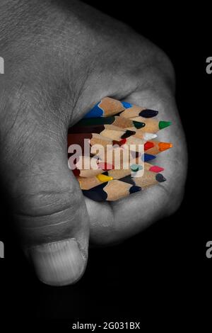 Colored pencils clenched in a fist, on a black background, close-up. Stock Photo