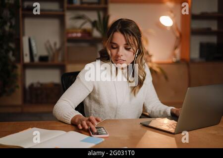 Serious businesswoman in earphones watching webinar on laptop making notes, learning studying computer course, making call, participating online confe Stock Photo