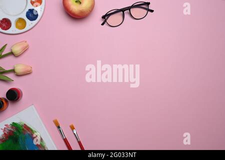 Top view artist workspace with color palettes, paint brushes, bouquet of pink tulips on pink pastel background. Stock Photo