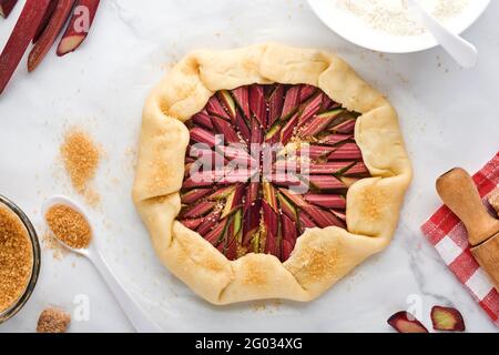 Galette with fresh rhubarb process of preparation and ingredients flour, water, butter, sugar and rhubarb for baking on white marble background. Chris Stock Photo