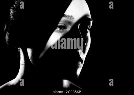 studio portrait of a beautiful young woman with shadows on her face, against dark backgroung. Black and white photo Stock Photo