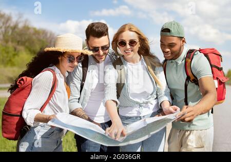 Local travel. Group of young people studying map on roadside, checking their destination point, hitchhiking for car Stock Photo