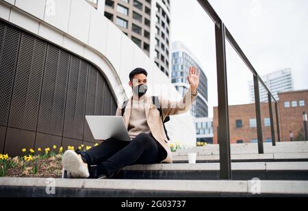 Happy man with laptop using laptop on the way to work outdoors in city, coronavirus concept. Stock Photo