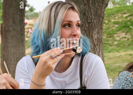 Young happy woman smiling and eating sushi in a park having picnic on a sunny summer day. Stock Photo