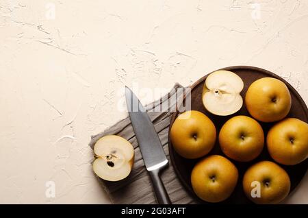 Asian pears with a silver knife on a wooden plate and a brown piece of cloth, on a light background. Stock Photo