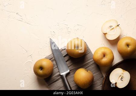 Asian pears with a silver knife on a wooden plate and a brown piece of cloth, on a light background. Stock Photo
