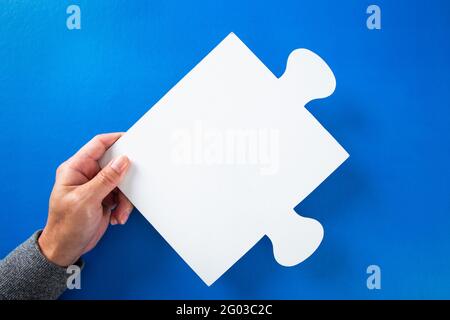 hands holding big paper white blank puzzles on a blue background, concept of business Stock Photo