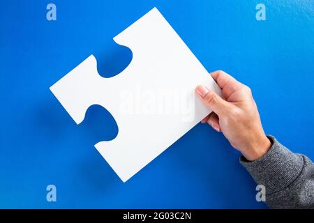 hands holding big paper white blank puzzles on a blue background, concept of business Stock Photo