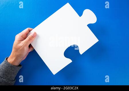 hands holding big paper white blank puzzles on a blue background, concept of business Stock Photo