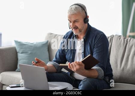 Happy old man having online class, using laptop and headset Stock Photo