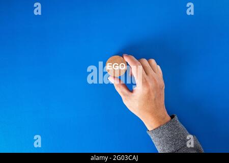 Businessman hand holding a round wooden block  with the word ego written on it. Stock Photo