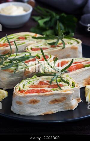 Rolls of thin pita bread and red salted salmon with lettuce leaves on a black ceramic plate, dark wooden background Stock Photo